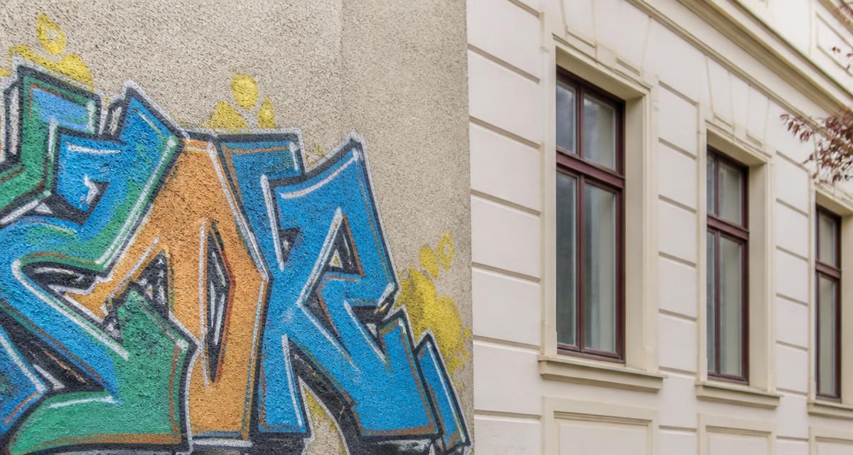 Großflächiges, mehrfarbiges Graffiti auf einer hellen Putzfassade eines Mehrfamilienhauses
